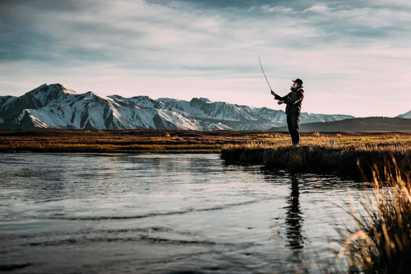 Angler casting a fly rod with snow-capped peaks behind