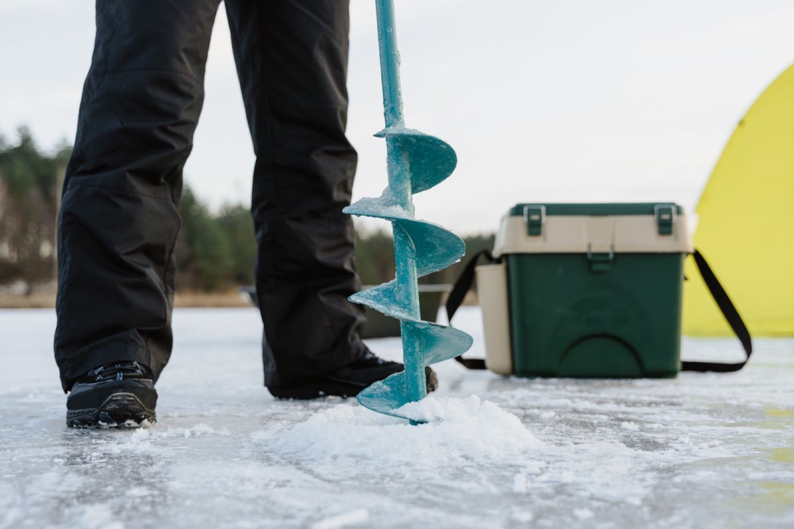 Ice auger, gear box and tent set up on a frozen lake