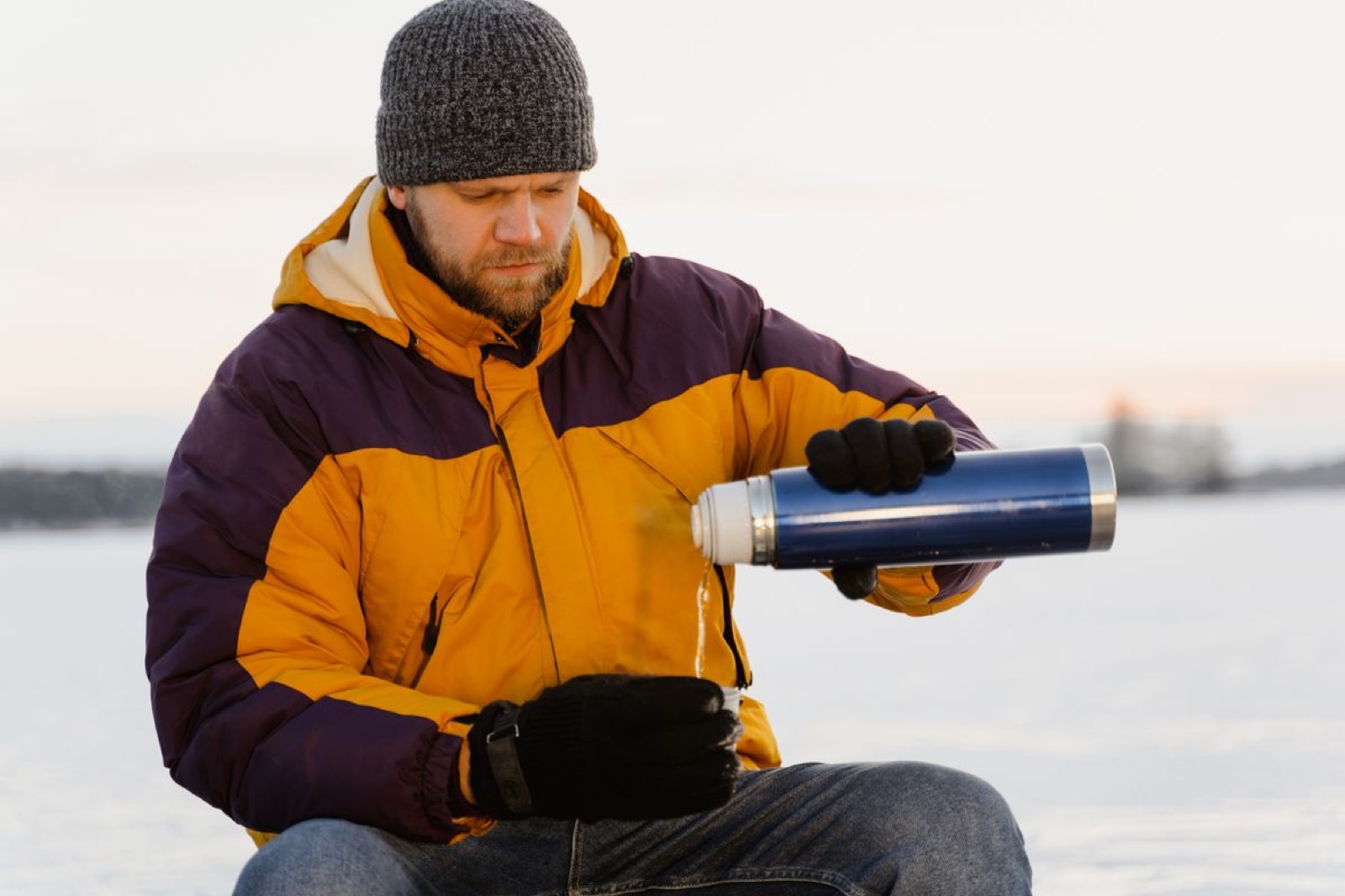 Guide pouring a hot drink from a thermos out on the ice
