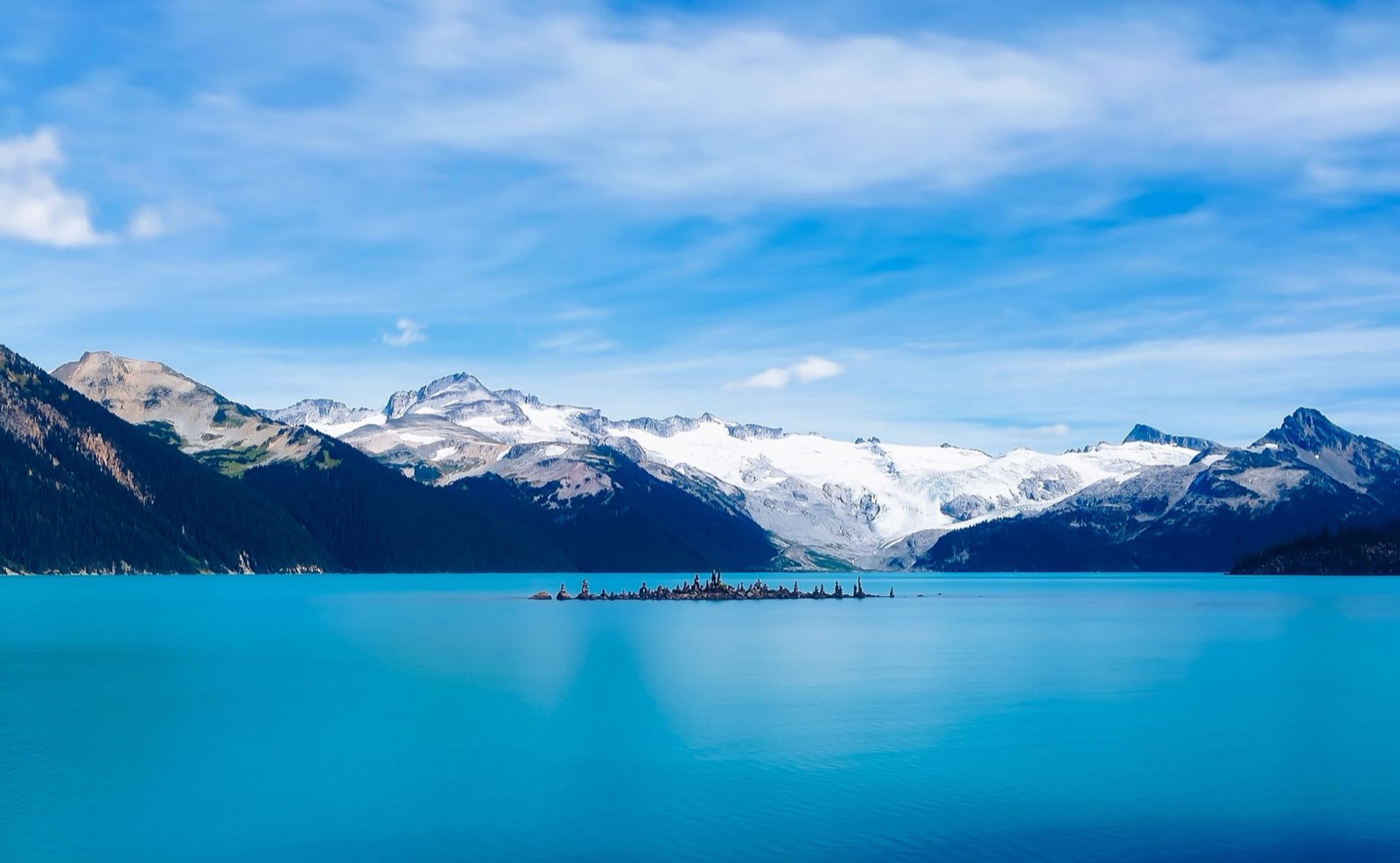 Bright turquoise lake below glacier-capped mountains in summer
