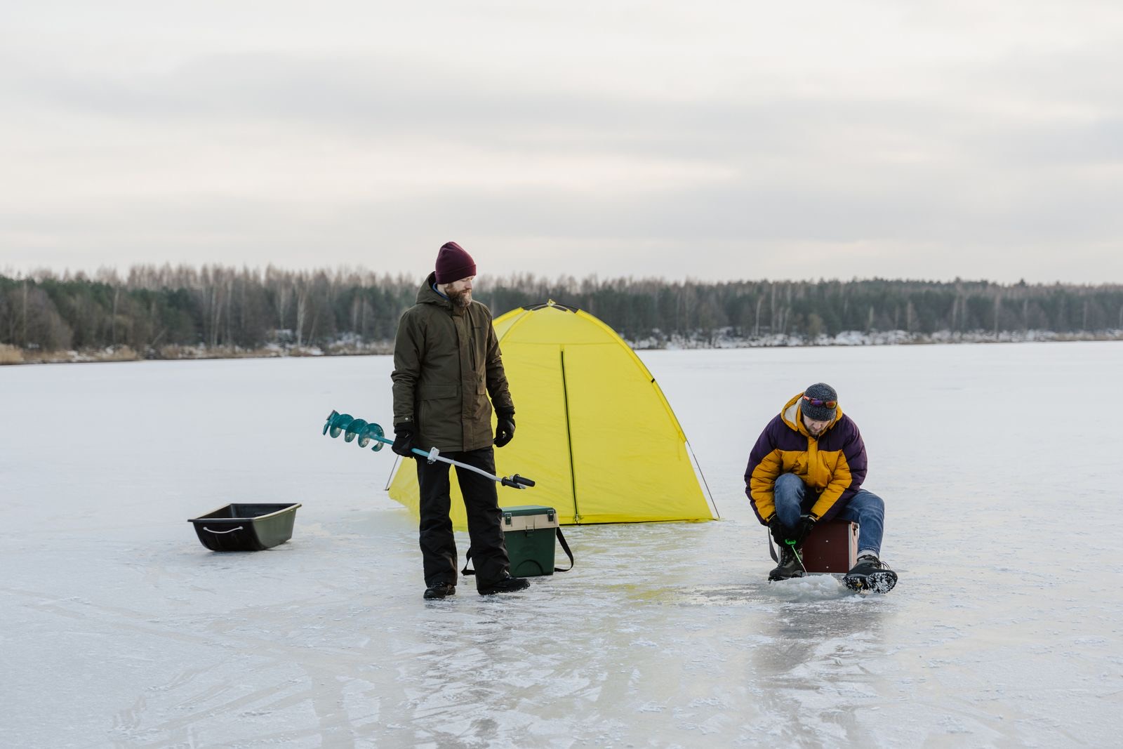 Guide setting up a tent, auger and gear on a frozen lake